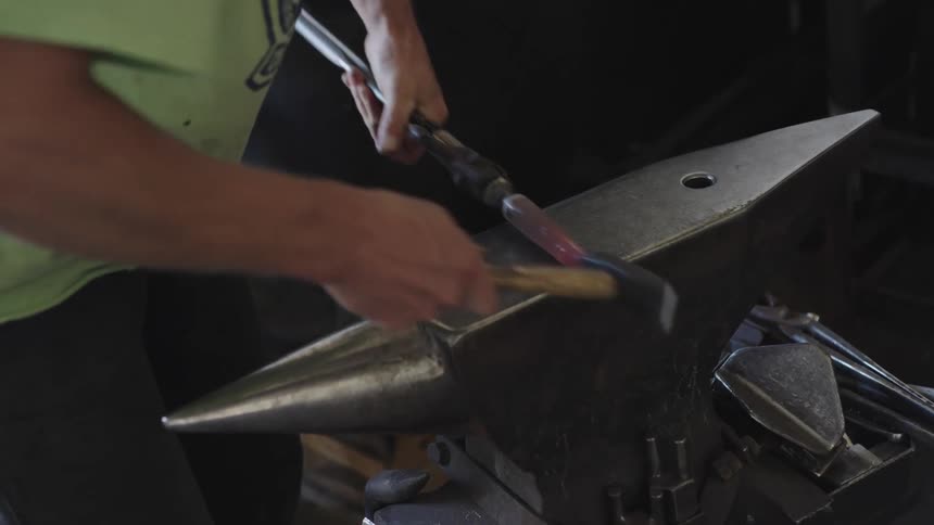 A blacksmith strikes a piece of redhot metal on an anvil