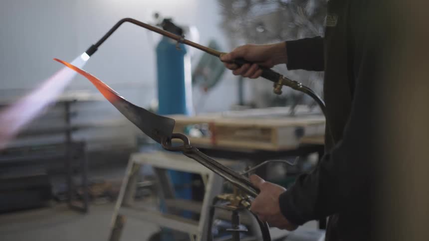 A blacksmith heats a twisted piece of metal with a blowtorch