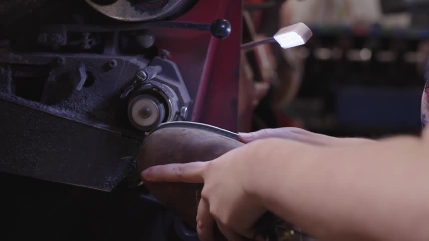 Hands shaping the sole of a leather shoe on a machine