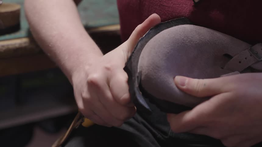 A white male uses a utility knife to trim part of a sole off of a pair of shoes