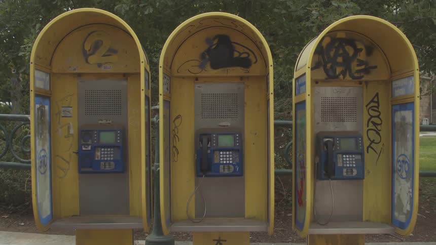 Three yellow payphones stand sidebyside each with graffiti on their surface