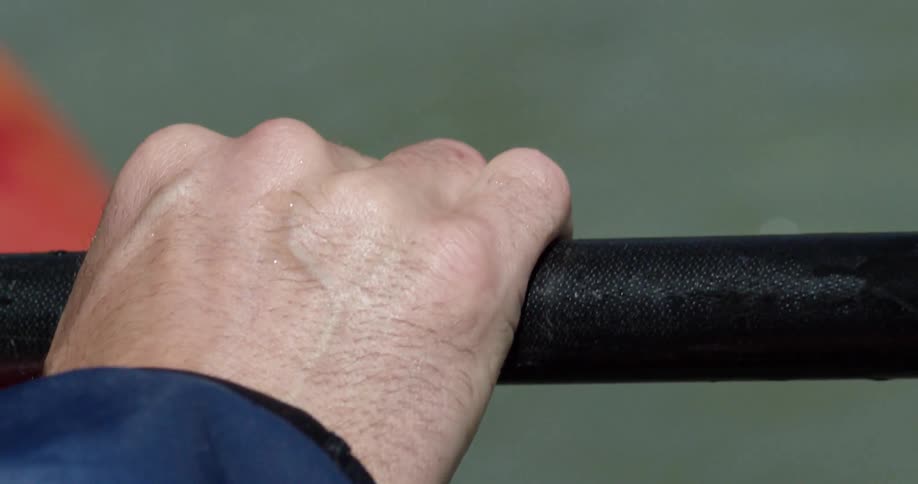 A hand holds onto a paddle on a river