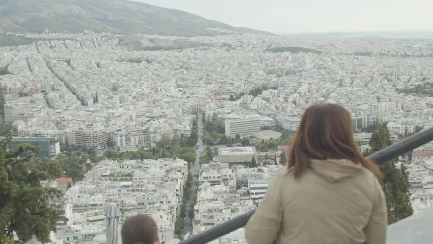 People on a tall ladder overlooking an urban city surrounded by mountains