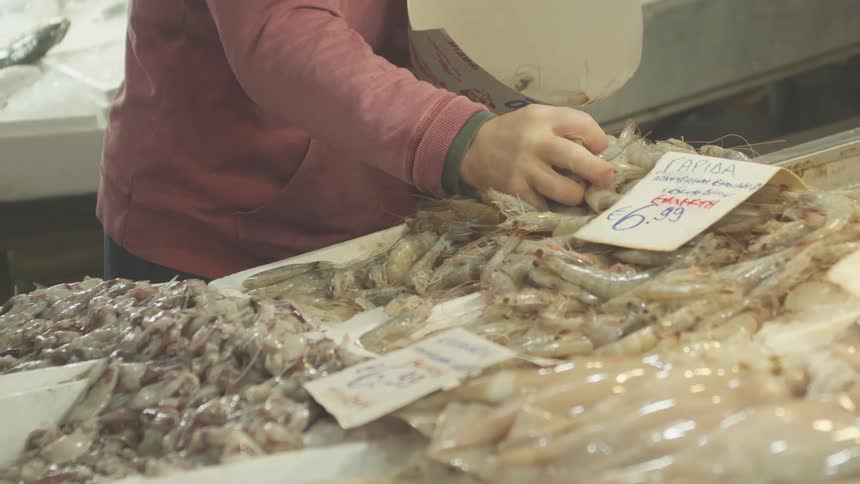 Person scooping up shrimp in carton at seafood market