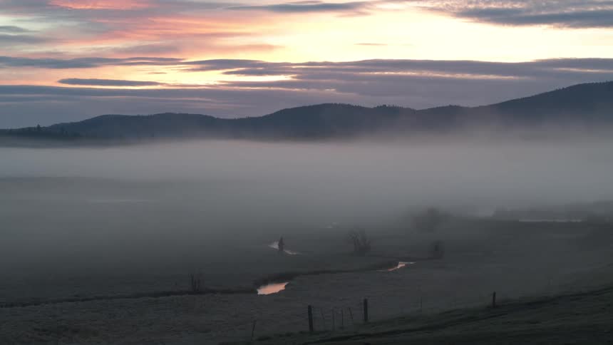 Aerial landscape of a green field with low fog and mountains on the horizon