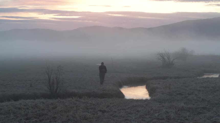 Person walking along a river on a foggy morning