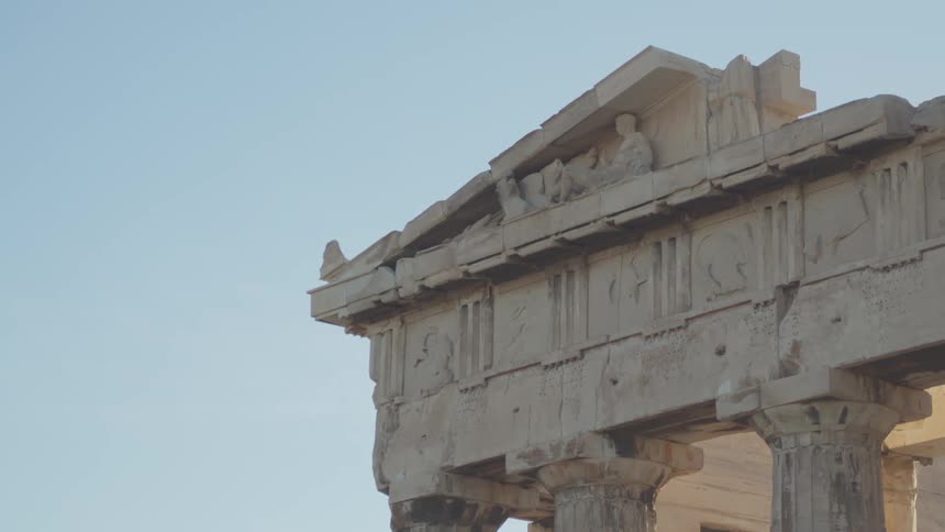 Ornate carvings adorn the top of a classical greek temple against a clear blue sky