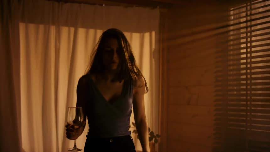 A woman dances alone in a cozy room holding a wine glass