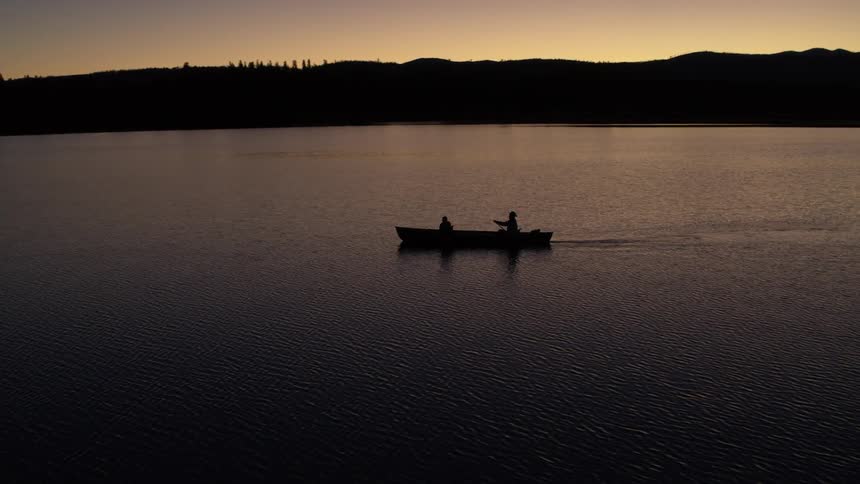 Two people paddle a canoe across a still lake at dusk