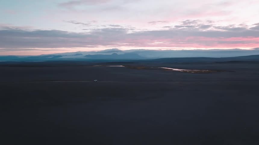 A solitary vehicle traverses the vast dark plain under a sky painted with the soft hues of twilight