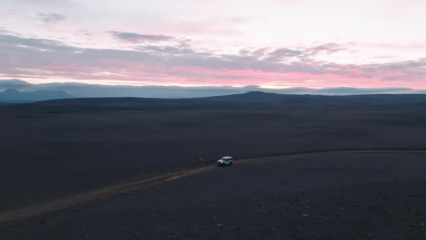 A car drives down a road in a desolate flat grasscovered area