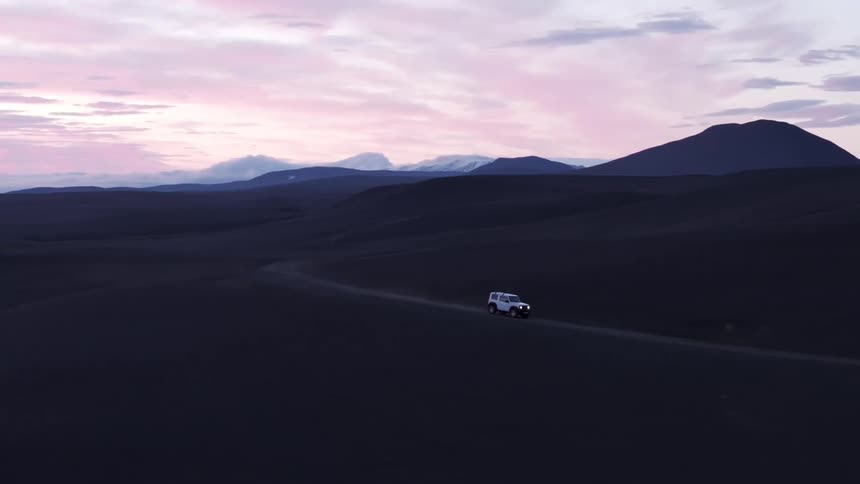 Aerial view of a white jeep traveling through a desert area on a purple sky morning