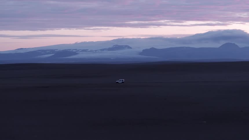 Aerial shot of a white vehicle traveling through a desert area with mountains in the background