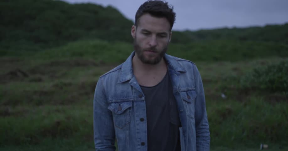 Man walking along a grassy field in a jean jacket