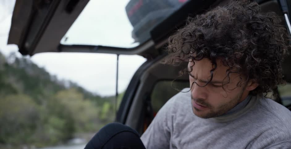 A man sitting on the trunk of his car tying his shoe