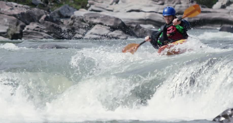A man paddles a kayak down a fast moving river