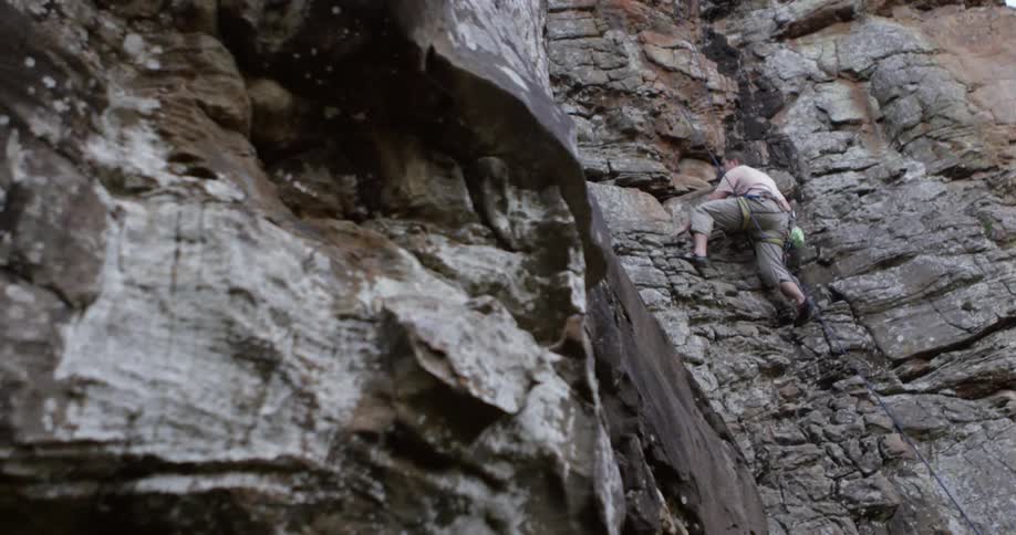 A rock climber is climbing up a cliff face