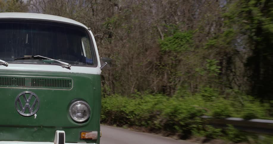 An old vw bus driving down a road in a forested area