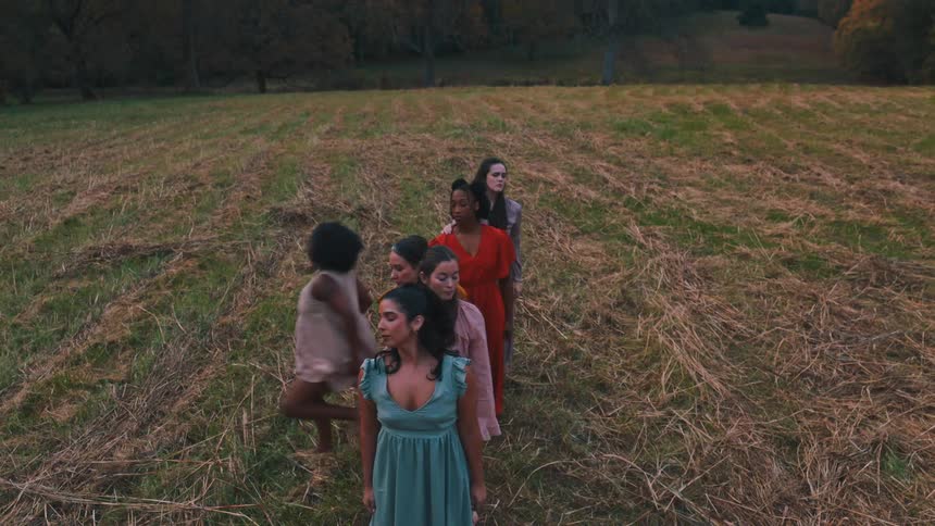 Women dancing together in a field with trees in the background