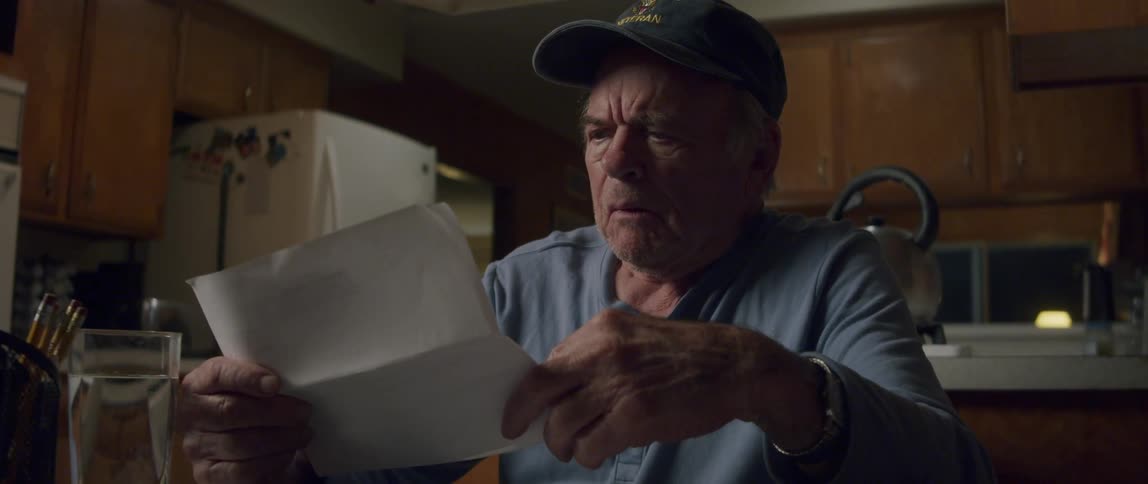 The elderly man sitting at the table opening a document and reading