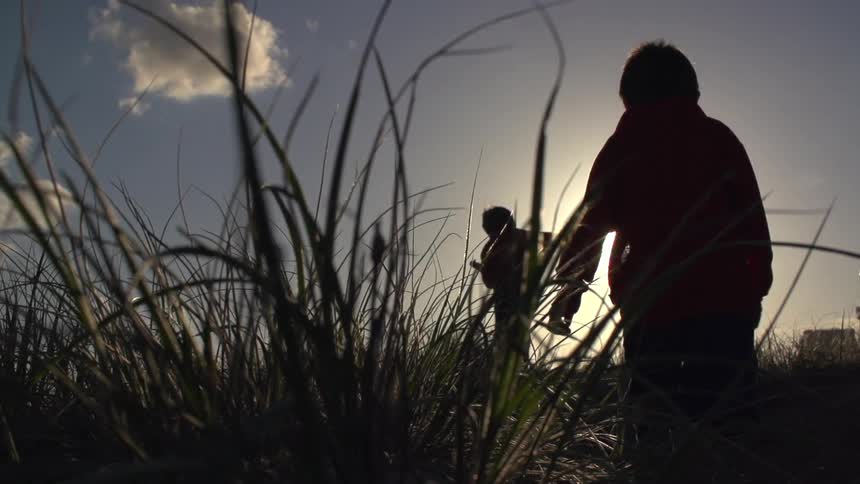 Two children running through a grassy field close to sunset