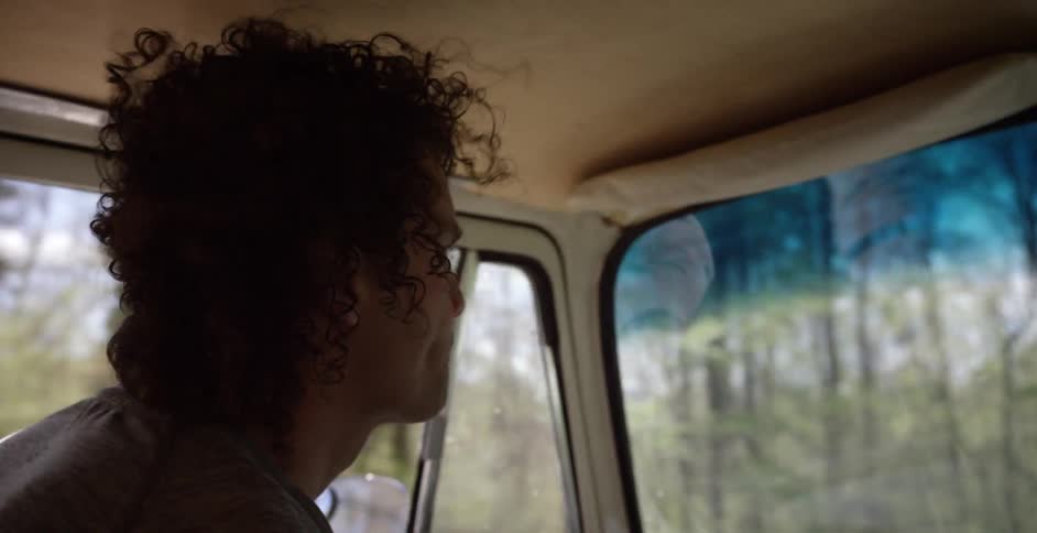 A man drives through a forested area with the window down