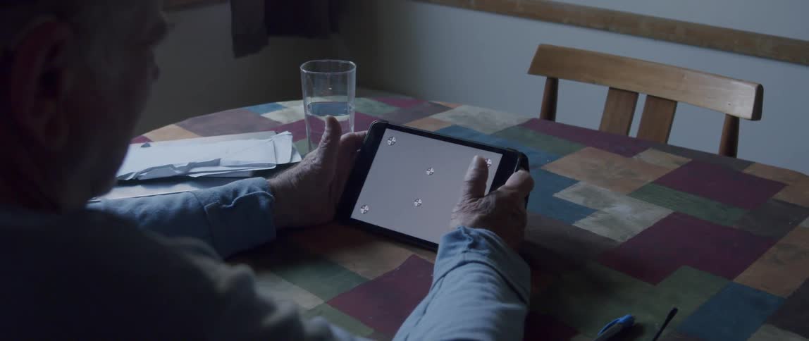 An elderly person sits at a table holding a tablet device with a replaceable screen