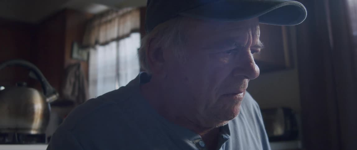 An elderly man looks disappointed or frustrated as he reads a letter