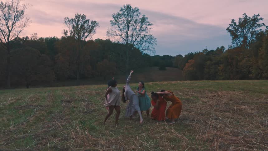 A group of women in flowing dresses perform a graceful dance in a field