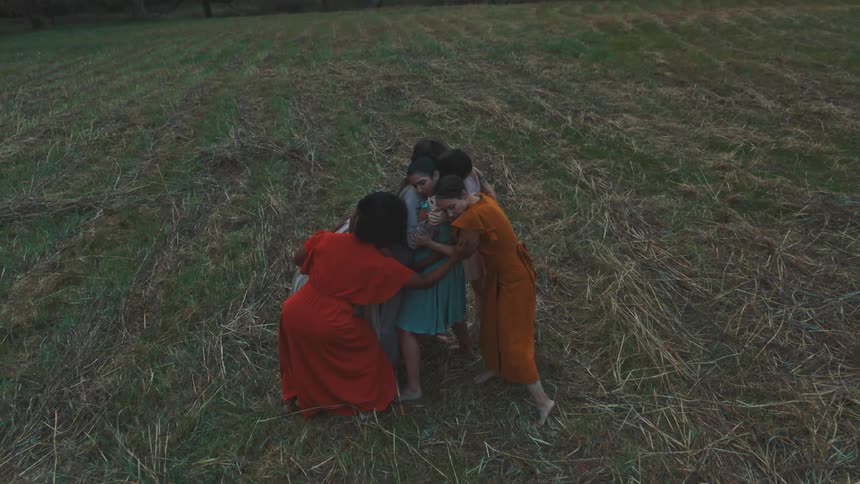 A group of women in flowing dresses perform a graceful dance in a field