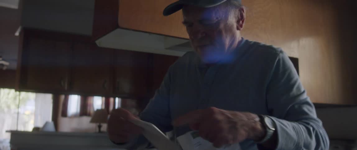 An elderly man stands up while sealing an envelope