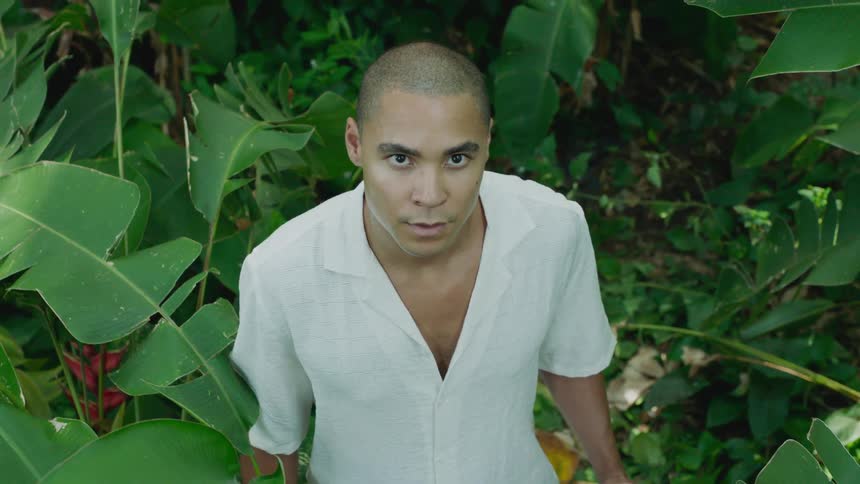 A man in a white shirt stops in the jungle to look up