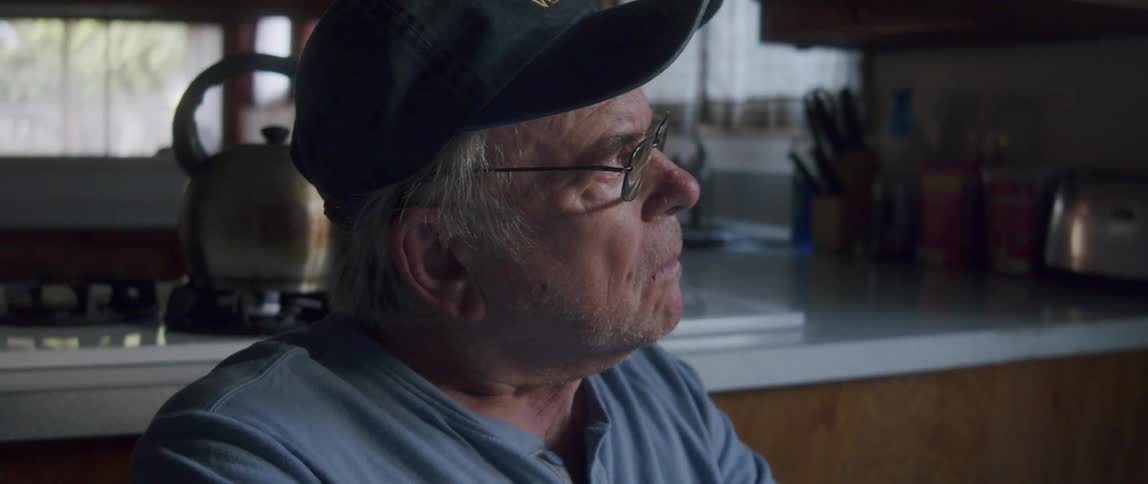 Elderly man in cap sitting putting on glasses