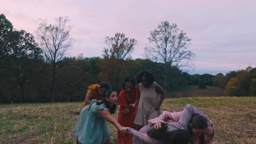 A group of women in flowing dresses perform a graceful dance in a field