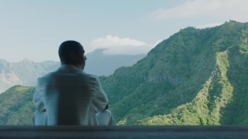 Man sitting facing a green mountain