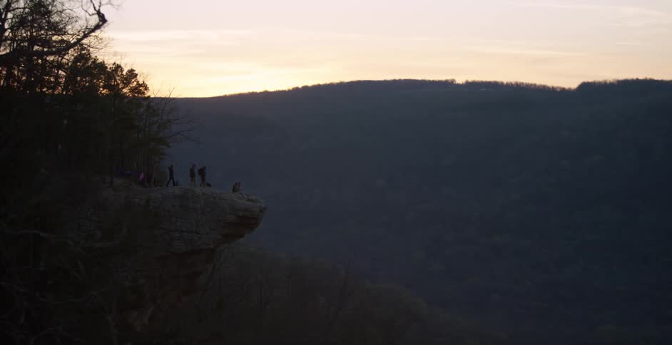A group of people watch a sunset from a rocky overlook
