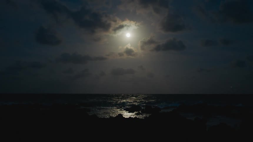 Moon shines brightly over the ocean at night reflecting in the water