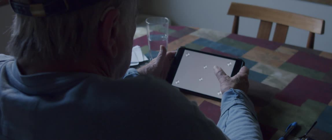 Elderly man sitting interacting with a tablet at the table