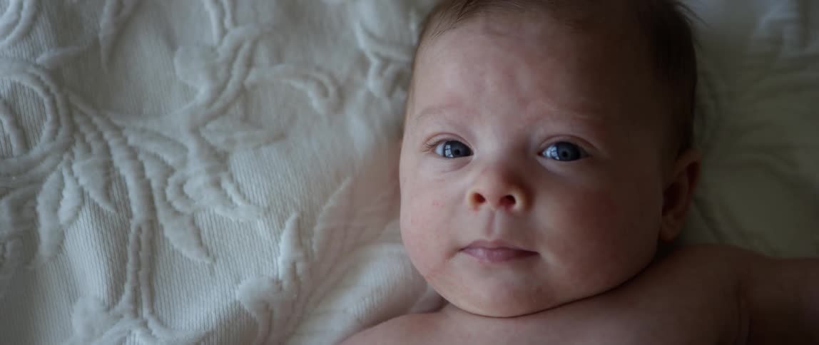 A baby laying on it's back and looking up at the camera