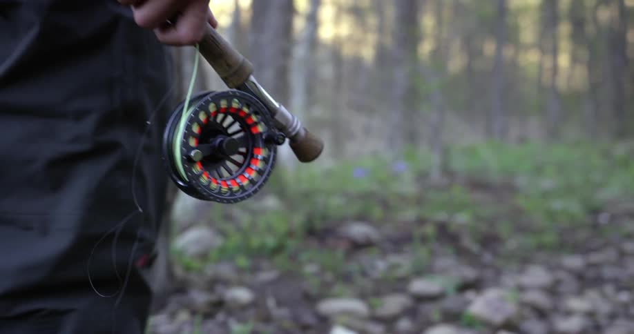 A person walks in the mountains carrying a fishing pole