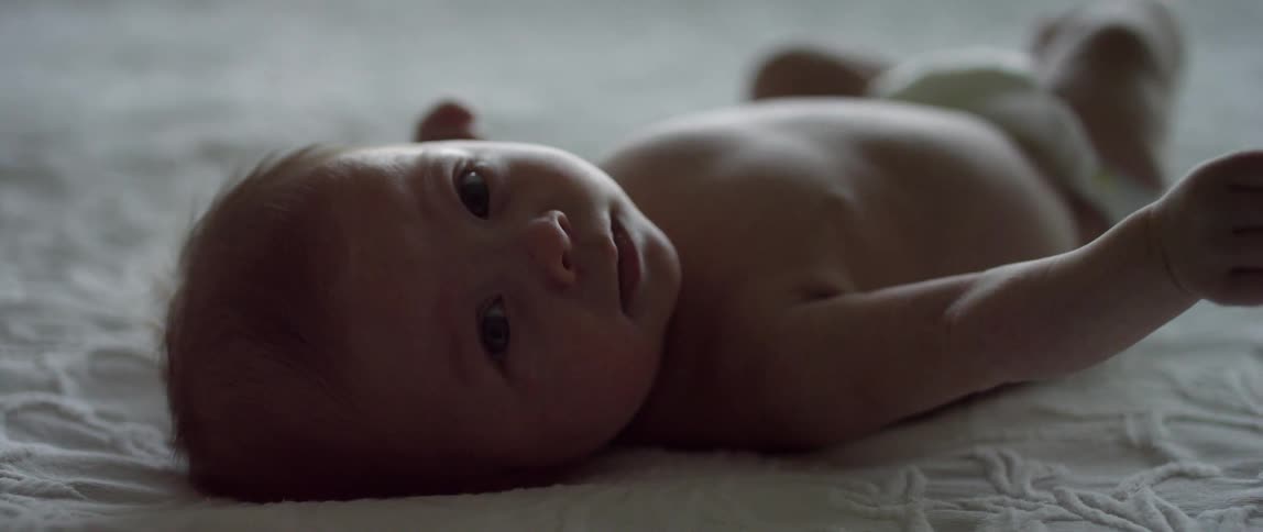 A baby squirms around on a white blanket