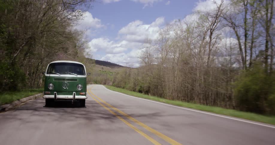 A volkswagen van drives through a forested area