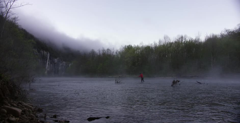A fisherman stands in the middle of a river