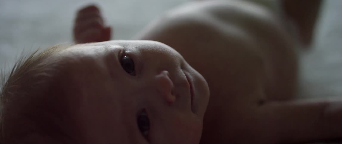 A baby is lying on the ground staring at the camera