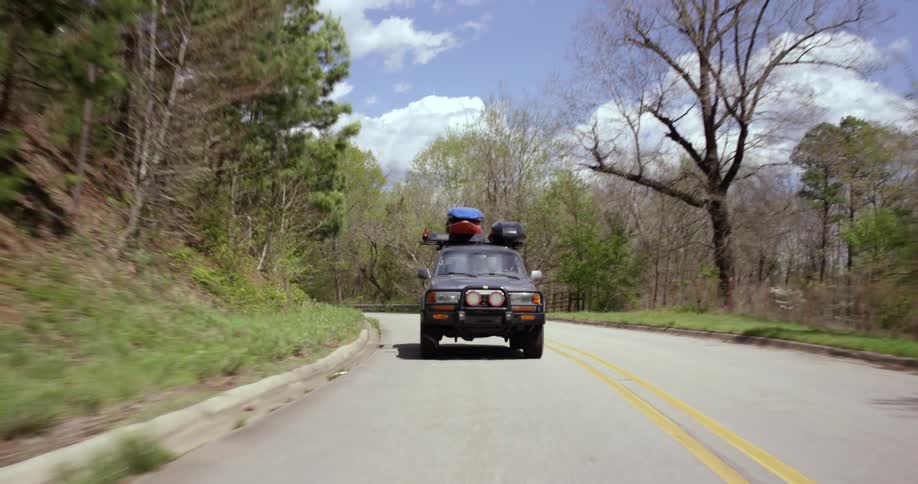 A car driving down the road on a sunny day with a kayak on top