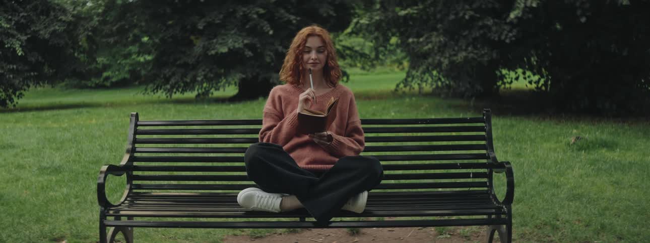 Woman sitting on a park bench writing in a journal