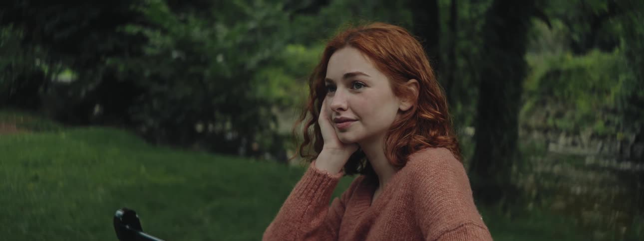 A teenage girl sitting on a bench smiles as she looks off into the distance