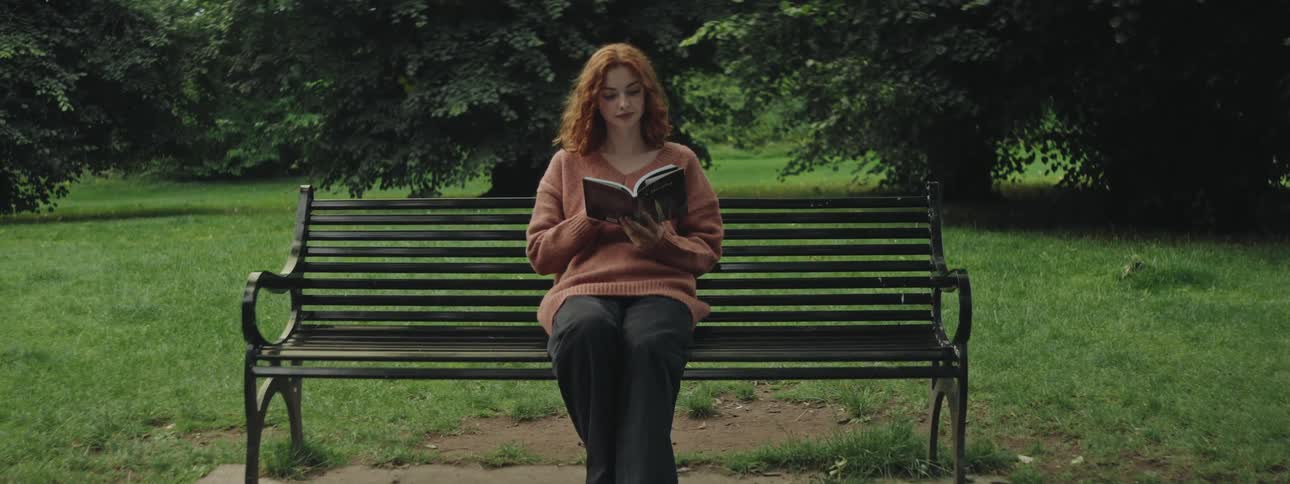 Young woman sitting on a bench in a natural area in daylight reading a book