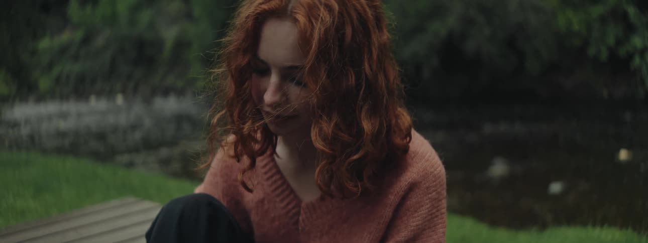 A teenage girl ties her shoe while sitting on a picnic table by a river