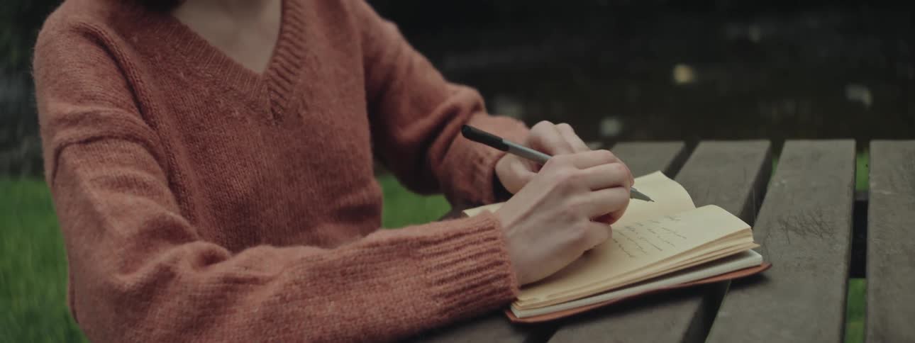Calm redhead woman sitting on a bench and writing in a notepad